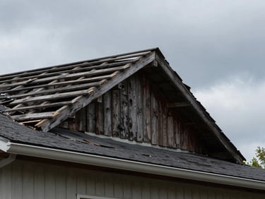 Dilapidated residential roof with water damage and sagging wooden rafters under overcast Ohio sky, gritty industrial photography