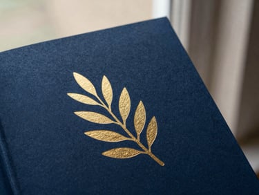 A beautifully designed book cover with minimalist gold foil olive branch illustration on a deep night-blue textured paper background, soft side lighting.