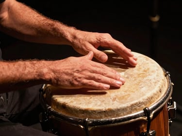 Close-up of hands playing a traditional Argentine bombo leguero drum under a warm copper spotlight