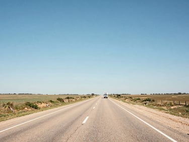A wide environmental shot of a long, straight rural Texas highway stretching to the horizon under a bright blue sky, a delivery vehicle in the distance.