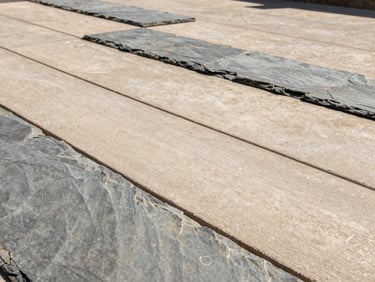 Macro architectural shot of a stamped slate patio finish, warm concrete and slate tones, crisp shadows under bright direct sunlight.