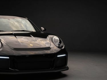 Low-key, high-contrast studio shot of a black Porsche 911 GT3, soft golden reflections on the metallic curves, dark minimalist background, negative space on the right.