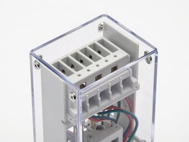 Isometric close-up of a modular thermoplastic electrical panel, transparent polycarbonate cover, clean wiring DIN rails inside, bright white background