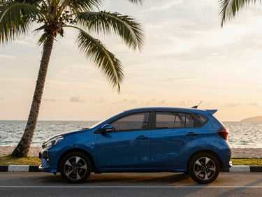 Medium-wide shot of a sleek blue Perodua Myvi parked along the scenic Kota Kinabalu coastal road at golden hour, with the South China Sea in the background, warm tropical sunlight.
