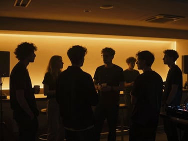 Dimly lit indoor networking area, silhouettes of music industry professionals talking, warm amber lighting