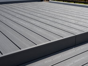 Wide environmental shot of a completed composite decking installation, charcoal-grey boards running parallel under flat north-facing daylight, clean fascia board detail at the deck edge, no people present