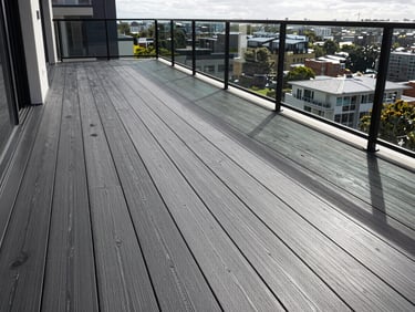 Wide environmental shot of a finished charcoal composite deck on a Melbourne residential balcony, clean board lines receding toward a railing, natural north-facing daylight, no people