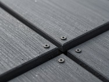 Extreme close-up of charcoal composite board junction and hidden fixing detail on a finished deck, controlled even lighting revealing grain texture and tight board gap, no people