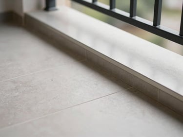 Close-up of a completed balcony renovation showing new large-format tiles meeting a clean aluminium threshold, grout lines sharp and even, controlled natural light from above, no people