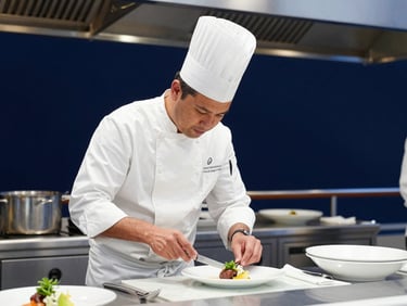 Professional maritime photography, a chef in an immaculate white uniform preparing dishes in a high-end cruise ship kitchen, bright natural daylight, deep navy tones, 35mm