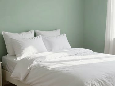 Bright interior photography of a neatly made bed in a tidy bedroom, soft morning sun, clean white linen, sage green accent wall, sharp focus, 35mm