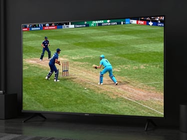 A modern smart TV screen glowing in a dark living room, showing a live cricket match in high definition, vibrant colors, cinematic lighting.