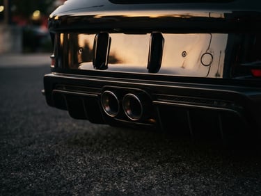 Tight detail shot of a modern Porsche 911 exhaust and rear diffuser, golden hour reflections on metallic dark paint, high-contrast shadows, cinematic 35mm, no people