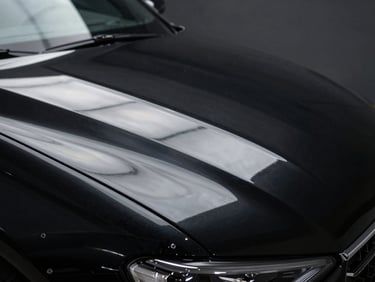 Macro shot of the exact same black car hood after multi-stage paint correction, showing a flawless mirror reflection of a single light source with zero swirl marks, deep obsidian paint