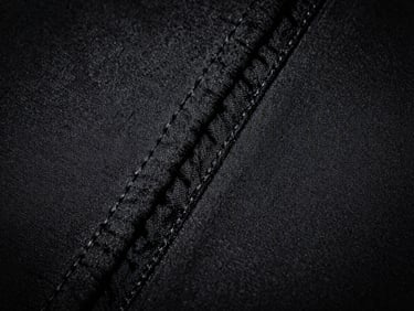 Macro close-up of technical athletic fabric weave, flatlock stitching, dramatic high-contrast studio lighting, stark monochrome tones, sharp focus