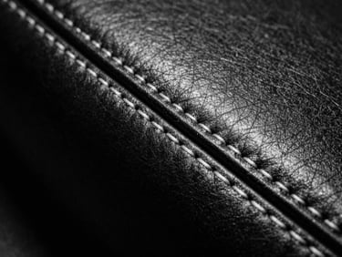 Macro detail shot of thick raw leather edge with heavy white technical stitching, dramatic studio lighting, stark monochrome