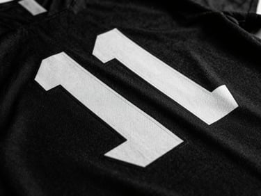 Close-up of sublimated team jersey fabric showing sharp graphics, high-contrast studio lighting, deep shadows, stark monochrome