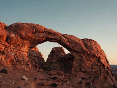 Dusty red sandstone arches in Arches National Park under a warm sunset sky, low-angle shot, cinematic travel style