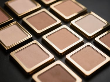 Close-up of luxury gold-trimmed cosmetic palettes arranged geometrically on a reflective black surface, dramatic low-key studio lighting, 35mm.