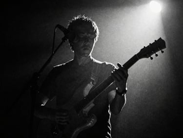 Gritty black and white cinematic film still of a musician performing under a harsh spotlight, deep shadows, heavy film grain, 35mm tri-x film.