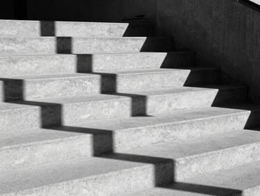 Abstract architectural shadows on a raw concrete staircase, direct midday sunlight, stark black and white composition, heavy grain.