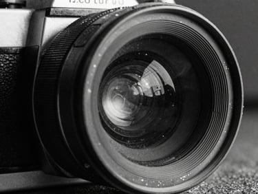 Extreme close-up of a gritty 35mm film camera lens, harsh direct sunlight reflecting off the glass, deep high-contrast shadows, heavy grain.