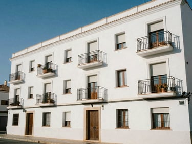 Exterior facade of a compact studio apartment block near Fuengirola beach, painted white, small juliet balconies, bright midday sun, street-level context with coastal light