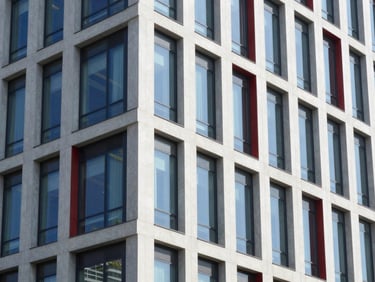 Modern commercial building facade with sharp architectural lines, glass windows reflecting daylight, clean finish