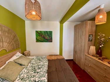 Bohemian bedroom interior with green walls, woven pendant lights, and botanical bedding.