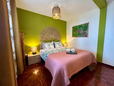 Tropical bedroom interior featuring a green accent wall, rattan headboard, and pink bedspread.