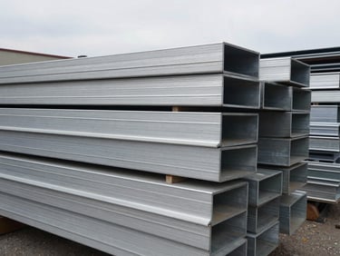 Stacked aluminum sheets and industrial scrap metal profiles, overcast outdoor light, raw texture.