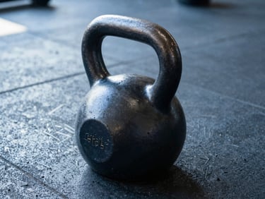 Close-up of a heavy steel kettlebell on a dark concrete gym floor, cool morning daylight.