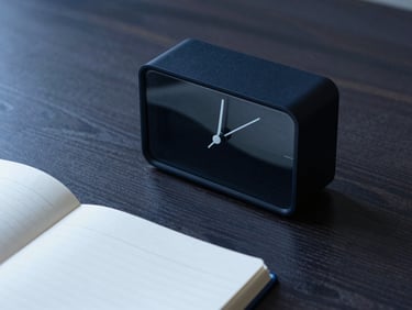 Sleek analog desk timer and open notebook on a dark wood desk, sharp shadows, 35mm lens.