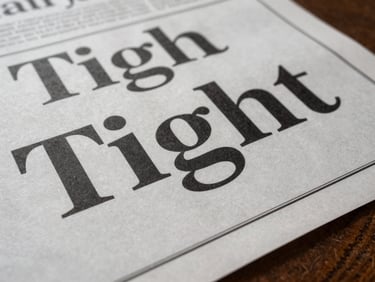 Tight studio detail — a broadsheet print advertisement laid flat under clean overhead light, financial brand typography clearly composed on the page surface, paper texture visible at edges