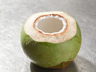 Macro commercial shot of a fresh green Nam Hom coconut sliced open, clear water glistening, bright tropical morning light, clean steel background, 50mm.