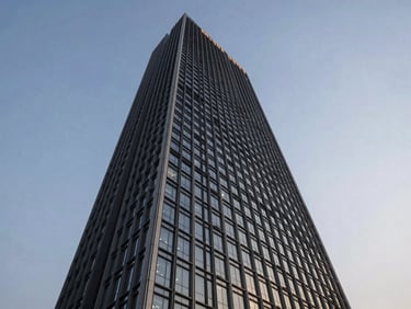 Dramatic low-angle view of One FNG tower in Sector 142 Noida, futuristic geometric facade against a clear evening sky with soft ambient lighting.