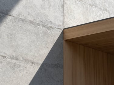 Tight abstract crop of raw concrete textured wall meeting smooth local timber paneling, harsh directional midday sunlight creating sharp geometric shadows.