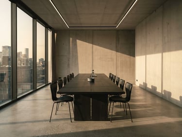 Minimalist wide architectural shot of a quiet, empty boardroom interior with a long dark oak table, sharp directional late-afternoon sun casting long geometric shadows on concrete walls, desaturated cool tones with warm undertones, 35mm lens.