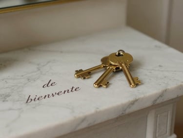 Détail tactile d'un accueil soigné, un trousseau de clés en laiton posé sur une cheminée en marbre à côté d'un mot de bienvenue écrit à la main.