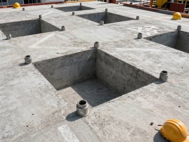 Overhead view of civil infrastructure work in a commercial building — concrete slab penetrations and conduit sleeves cast in place, hard-hat zone markings visible on concrete floor, industrial daylight, no people in frame