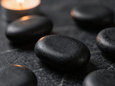 Macro close-up of smooth black basalt stones resting on dark textured marble, soft ambient lighting, 35mm