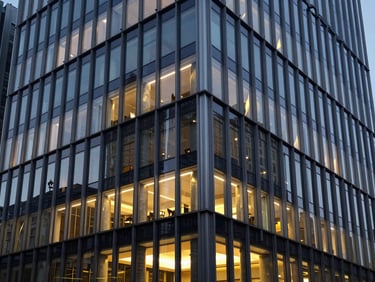 Architectural close-up of a modern corporate trade headquarters in Budapest, sharp steel and glass facade reflecting cool evening light with warm interior gold highlights, 35mm