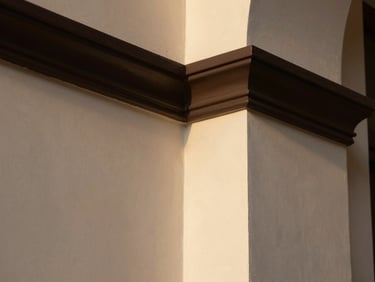 Macro architectural detail shot of crisp dark paint edges meeting warm off-white plaster, sharp focus, natural side lighting.