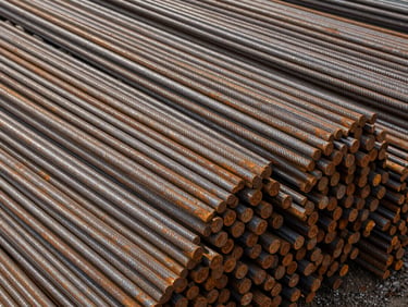 Close overhead shot of bundled TMT steel rods stacked in a storage yard, site daylight, rust-free ribbed surface texture visible, no people