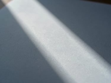 A close-up of fine textured paper with abstract geometric shadows from a window, soft daylight, low contrast, minimalist editorial photography