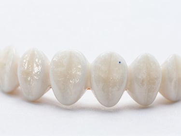 Extreme close-up of hand-finished ceramic veneers resting on a pristine white surface, highlighting natural light transmission and texture