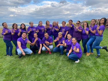 A large group of people wearing purple t-shirts posing on a grassy hill for awareness.