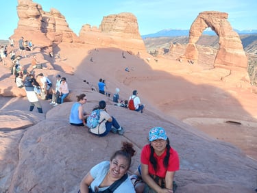 Tourists gathering on red rock formations at Delicate Arch in Arches National Park, Utah.