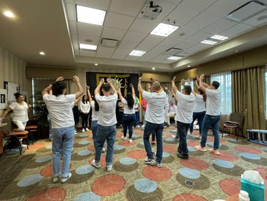 A group of people wearing white shirts and jeans participating in a team-building workshop activity in a conference room.