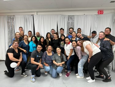 A large, diverse group of smiling people posing for a community group photo in front of white curtains.